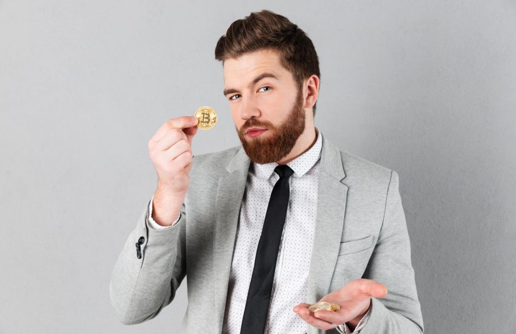 A man is holding a Bitcoin coin in one hand to start Bitcoin trading