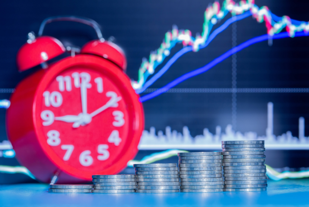 Cinco pilas de monedas y un reloj despertador con un gráfico de velas de fondo