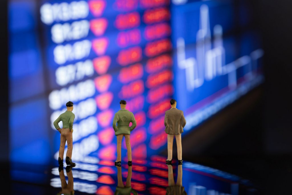 Tres figuritas de plástico en forma de personas frente a pantallas gigantes de scalping en binance