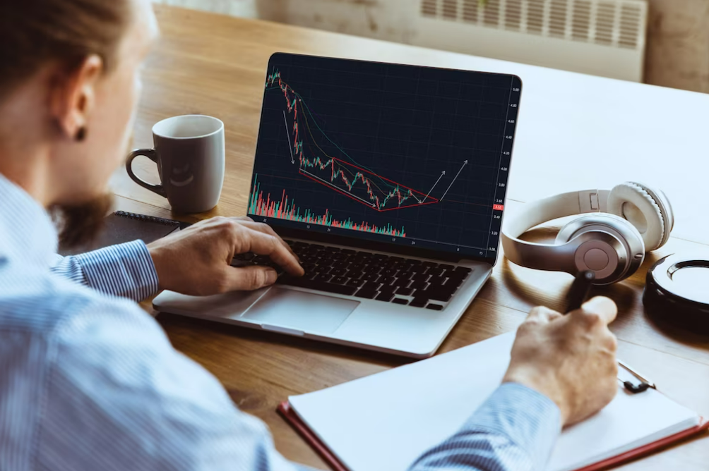 Man writing in a notebook and analyzing price charts on a computer to learn to trade.