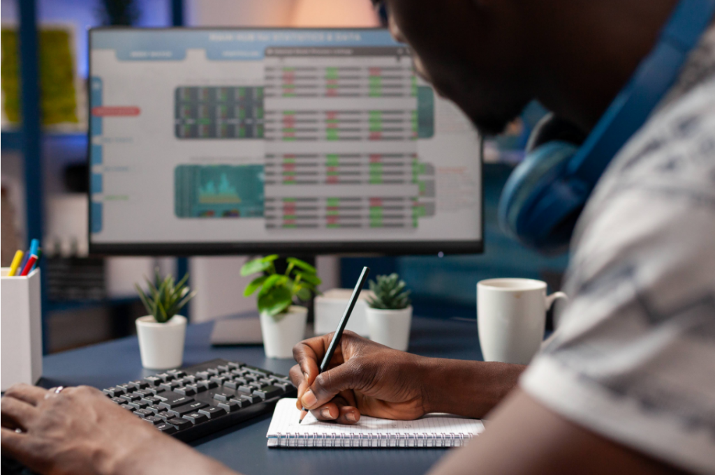 Man writing in his notebook and looking at his computer screen trading images